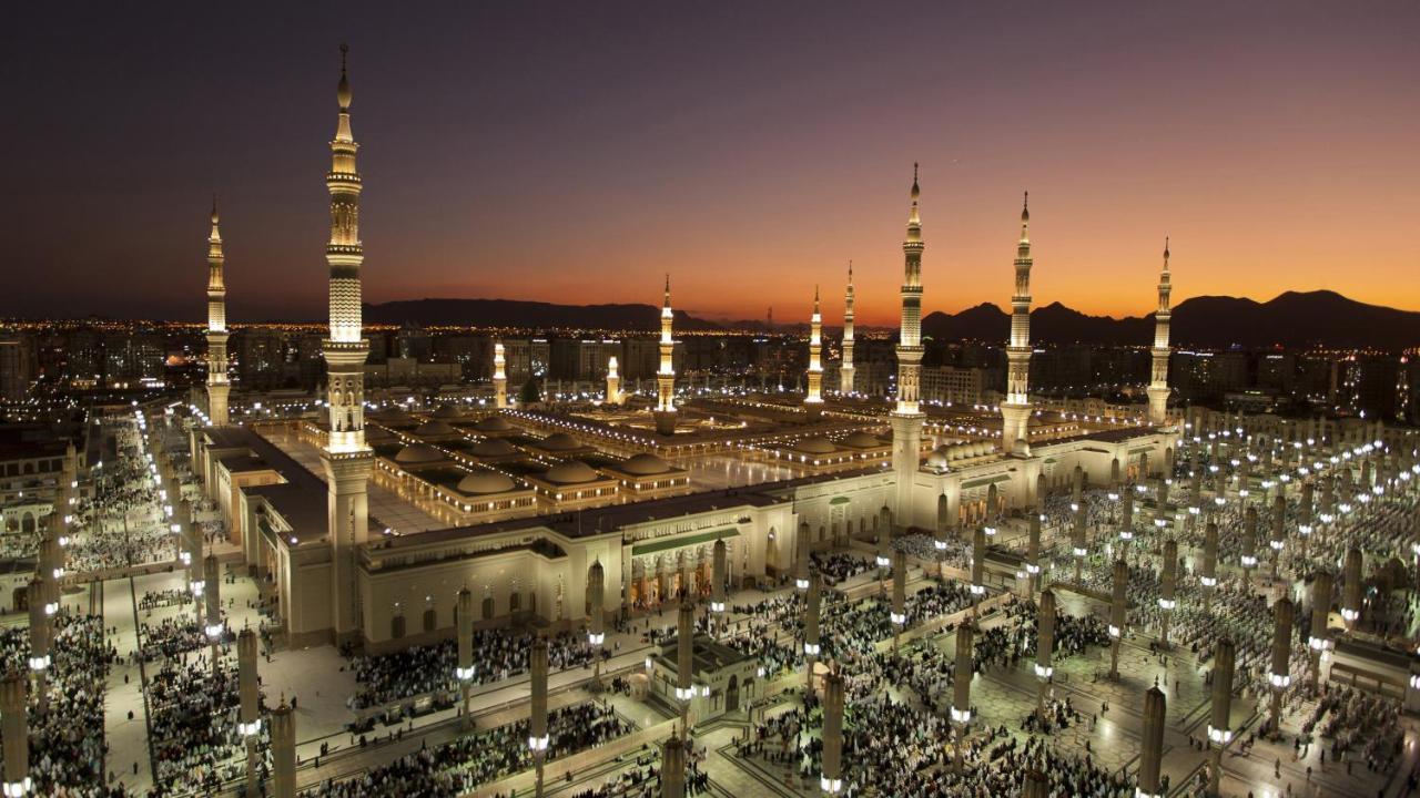 Hotel Intercontinental Dar Al Iman Madinah By Ihg Medyna Zewnętrze zdjęcie The photo depicts an aerial view of a large mosque complex during sunset. The mosque features multiple tall minarets, which are intricately designed and illuminated, giving the scene a stunning appearance as the sky transitions from daylight to dusk.
