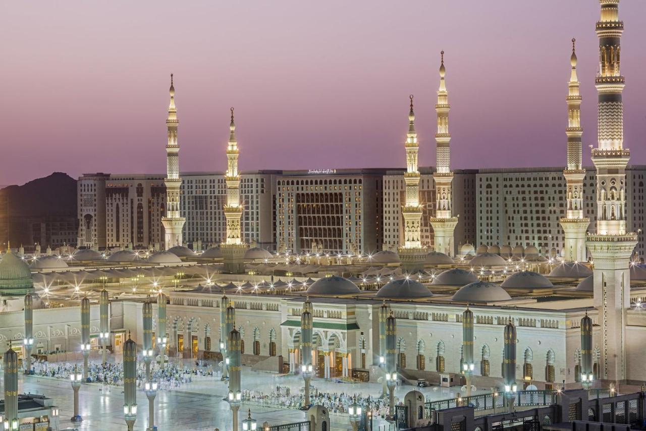 Hotel Intercontinental Dar Al Iman Madinah By Ihg Medyna Zewnętrze zdjęcie The photo shows a view of an expansive mosque complex, featuring several tall minarets that are illuminated against a twilight sky. The structure appears grand and is likely adorned with intricate architectural details. There are people gathered in t
