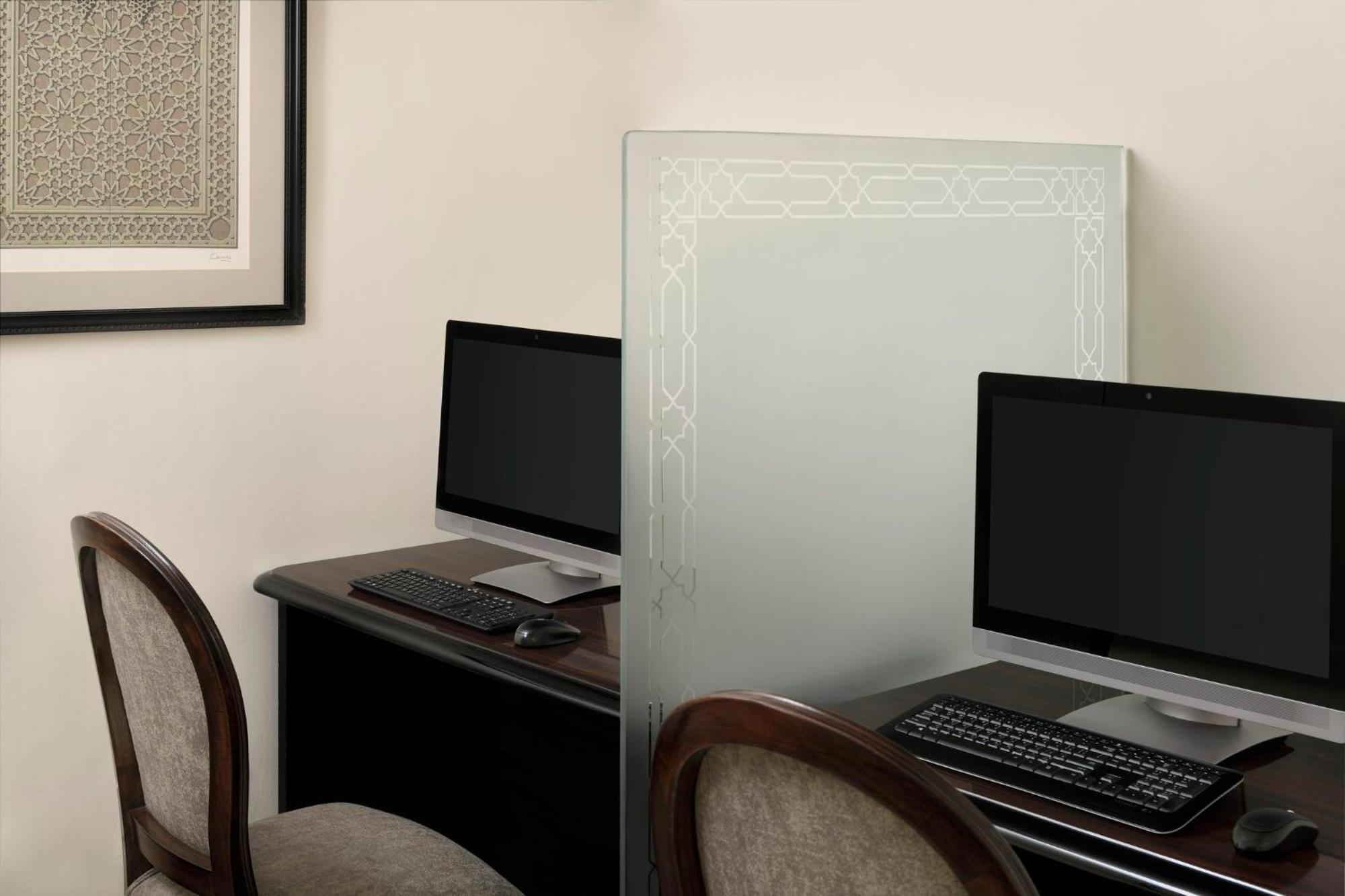 Hotel Intercontinental Dar Al Iman Madinah By Ihg Medyna Zewnętrze zdjęcie The photo shows a small office or workspace area featuring two computer stations. Each station has a black monitor, a keyboard, and appears to be set up on a dark wooden desk. A translucent glass partition is placed between the two workstations, prov