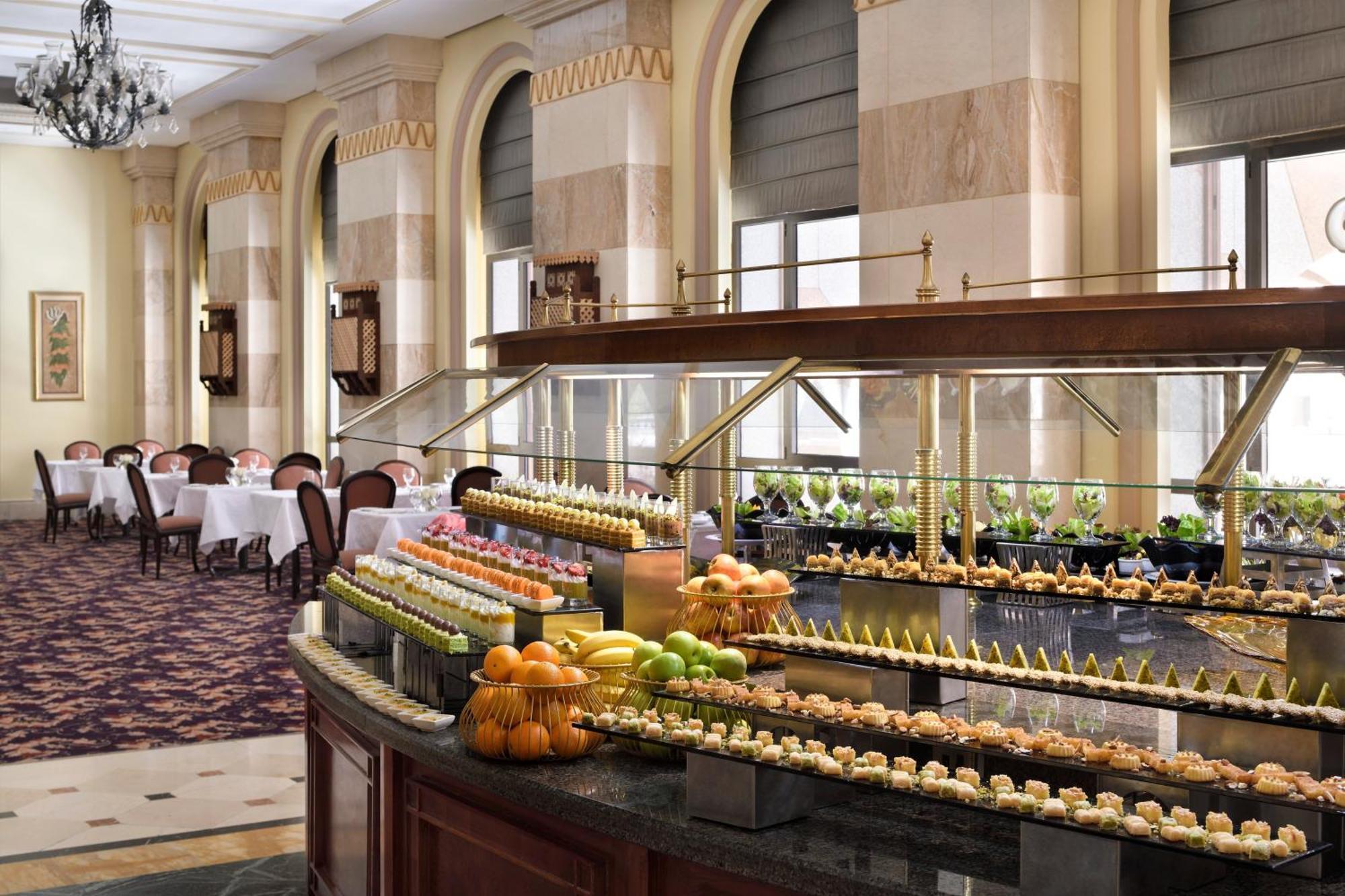 Hotel Intercontinental Dar Al Iman Madinah By Ihg Medyna Zewnętrze zdjęcie The photo depicts an elegant dining area featuring a buffet-style display. In the foreground, a beautifully arranged buffet counter showcases an array of desserts, including miniature pastries and colorful fruit. The setting has a sophisticated ambia