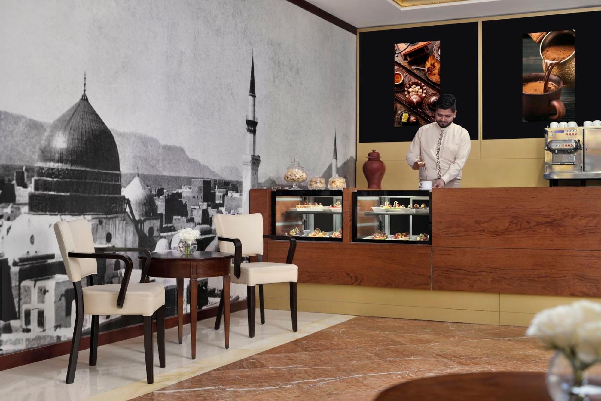 Hotel Intercontinental Dar Al Iman Madinah By Ihg Medyna Zewnętrze zdjęcie The photo shows a stylish interior of a café or pastry shop. In the background, there is a large black-and-white mural depicting a cityscape, featuring a prominent dome and minaret, suggesting an architectural style that could be from a Middle Easter