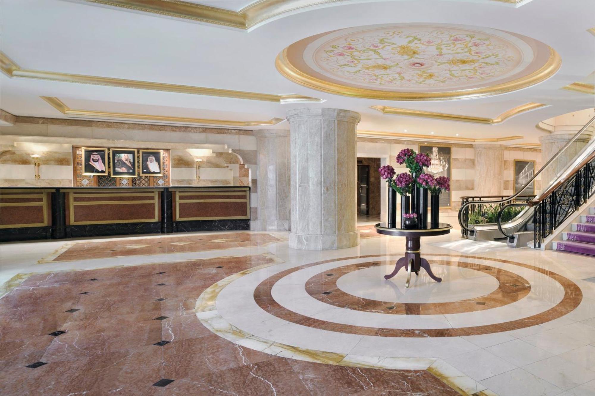 Hotel Intercontinental Dar Al Iman Madinah By Ihg Medyna Zewnętrze zdjęcie The photo shows a luxurious hotel lobby. The space features elegant marble flooring with circular designs, complemented by a large, decorative ceiling. In the center, there is a round table adorned with a floral arrangement. Behind the table, a recep