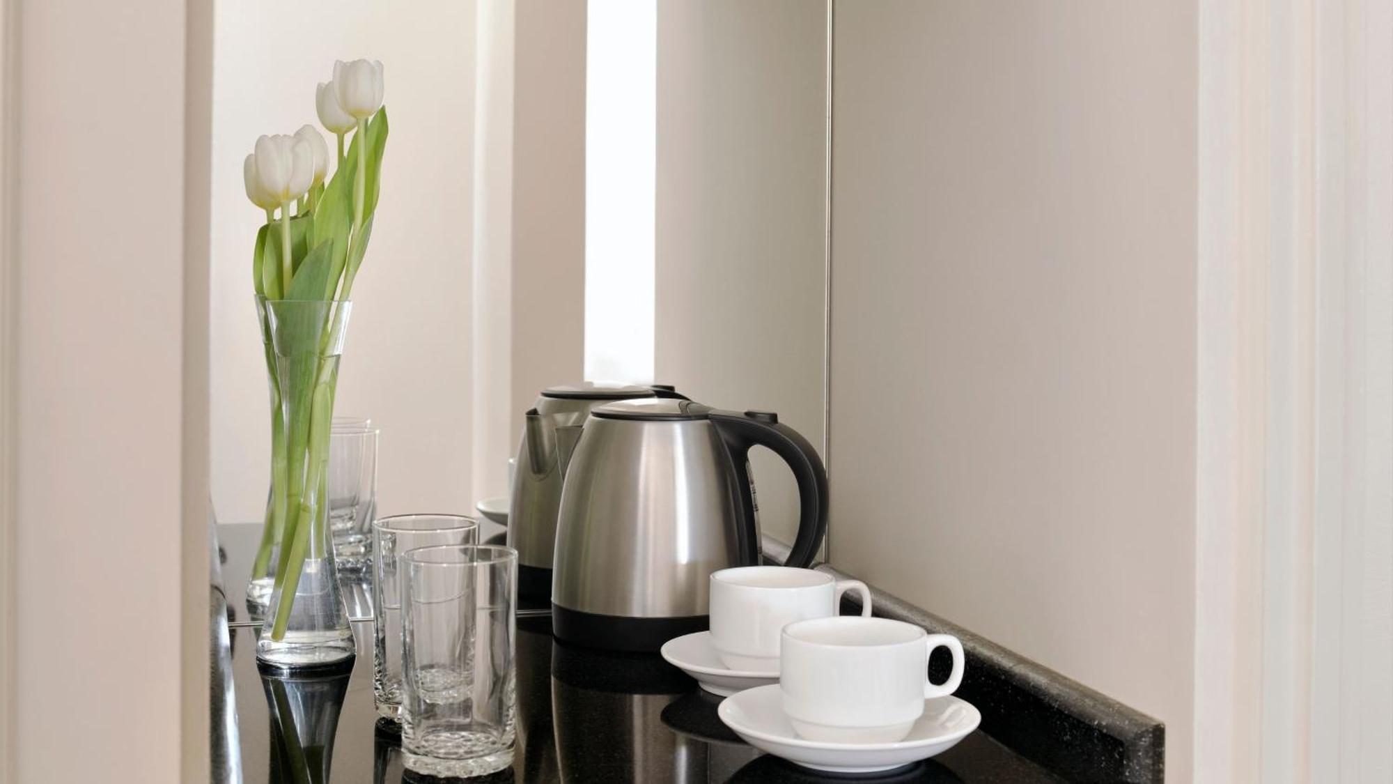 Hotel Intercontinental Dar Al Iman Madinah By Ihg Medyna Zewnętrze zdjęcie The photo depicts a neatly arranged beverage area. In the foreground, there are two white coffee cups on small saucers. Next to them, there are two clear drinking glasses. In the background, there is a silver electric kettle, which is positioned next