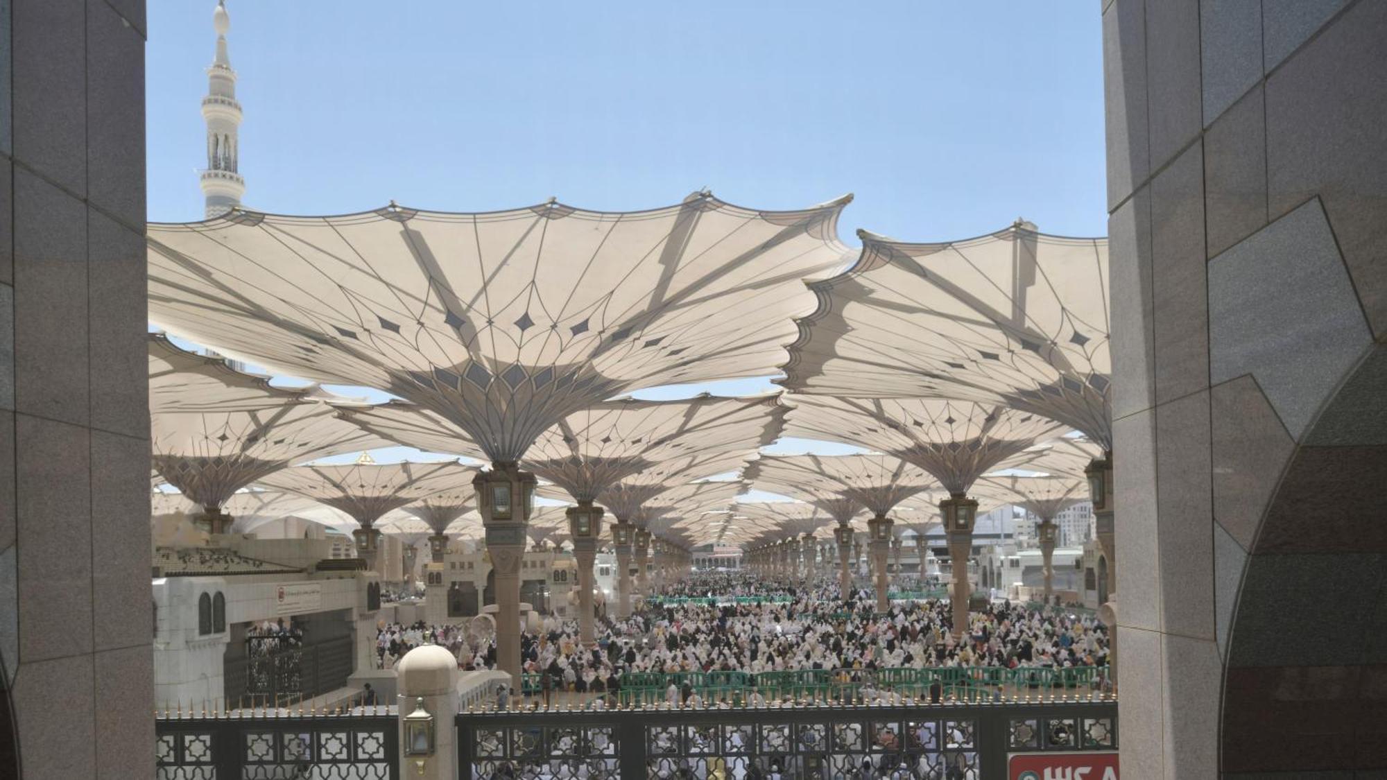 Hotel Intercontinental Dar Al Iman Madinah By Ihg Medyna Zewnętrze zdjęcie The photo shows a large open area covered by expansive canopies, likely designed to provide shade for the people below. Underneath the canopies, there are many individuals gathered, possibly participating in a religious event or gathering. In the bac