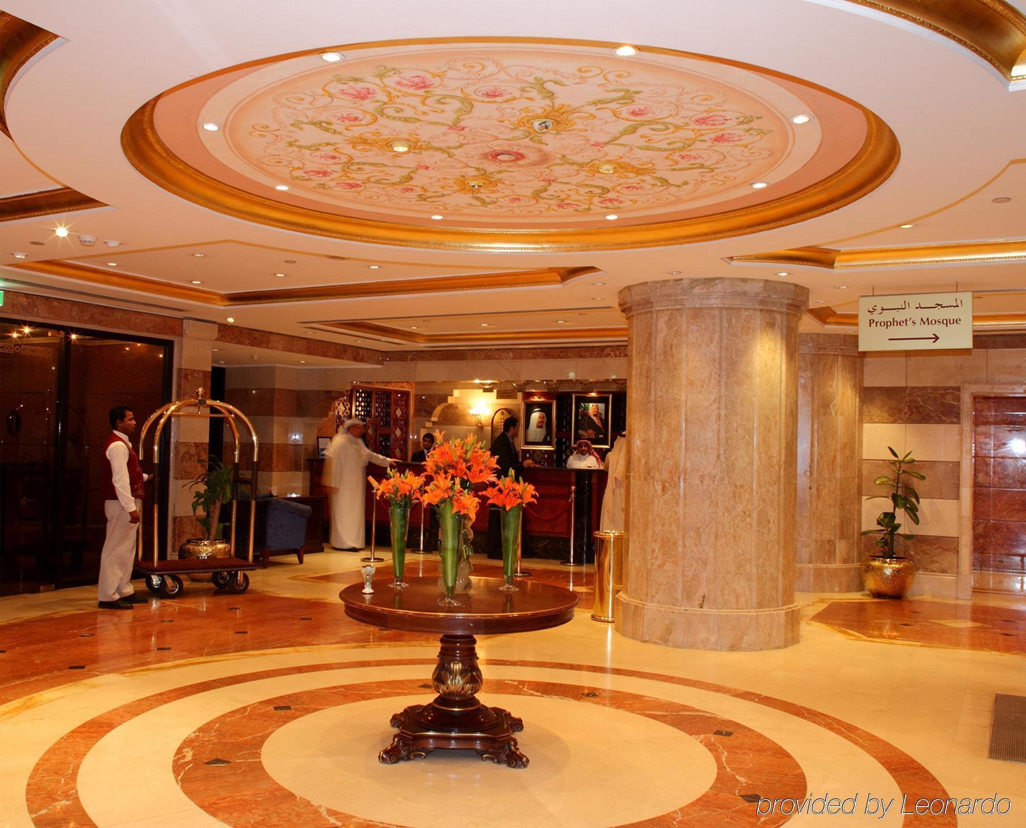Hotel Intercontinental Dar Al Iman Madinah By Ihg Medyna Wnętrze zdjęcie The photo depicts a luxurious hotel lobby. The ceiling features an ornate design with floral patterns, adding elegance to the space. In the center of the lobby, there is a decorative table with a bowl or vase of bright orange flowers. The flooring is