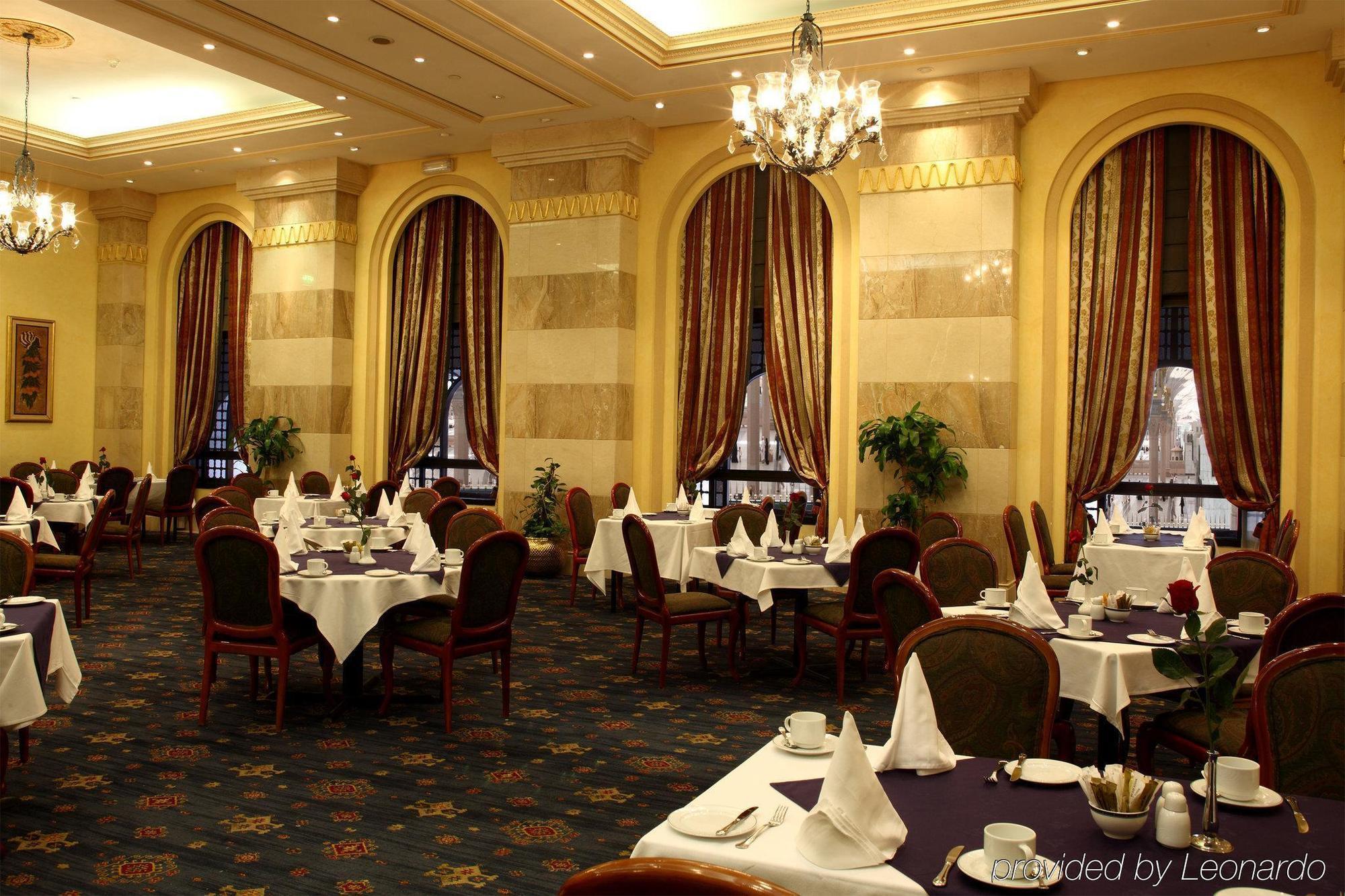 Hotel Intercontinental Dar Al Iman Madinah By Ihg Medyna Restauracja zdjęcie The photo depicts an elegant restaurant interior. The space features ornate decor with tall windows draped in rich, patterned curtains. Tables are neatly set with white tablecloths and napkins, and there are plush chairs arranged around them. The flo